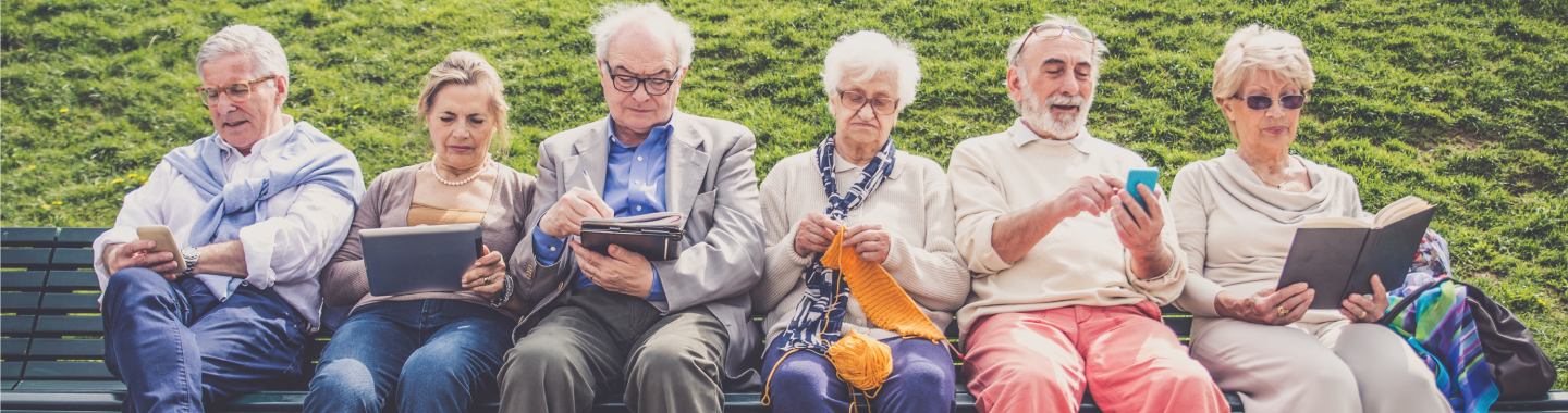 Older people sitting on bench reading and knitting.