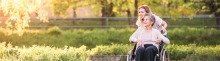 Daughter pushing her mother in a wheelchair in nature